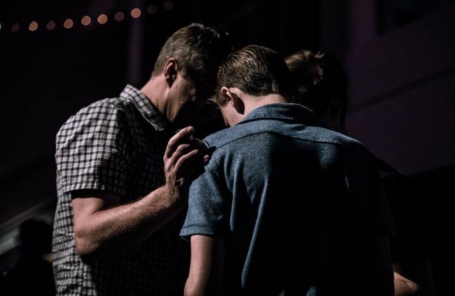 Three people are held together in prayer supporting one another