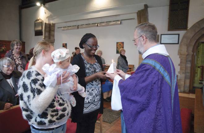 A vicar gives a candle to a godparent