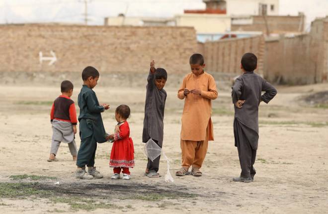 Six children in Kabul, Afghanistan play with a kite outside of an urban centre.