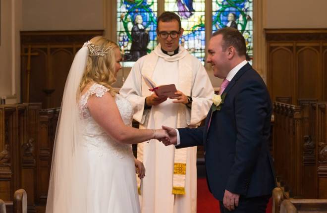 A bride and groom join hands in front of the vicar