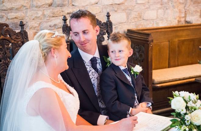 Bride and groom signing the register with their son on his dad's knee