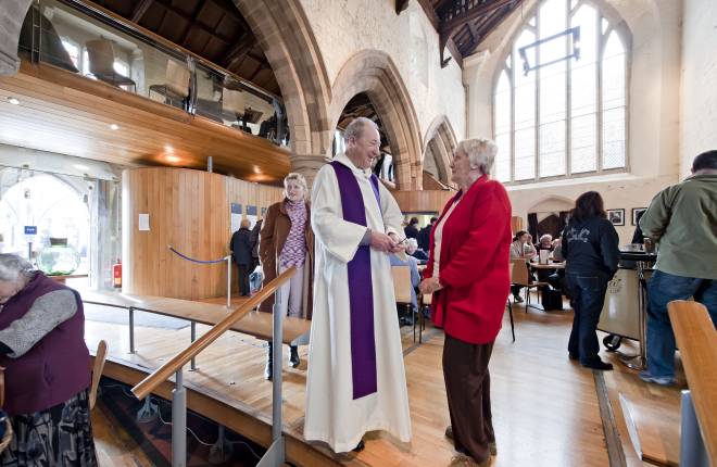 A vicar speaks to a woman in a coffee area of a church