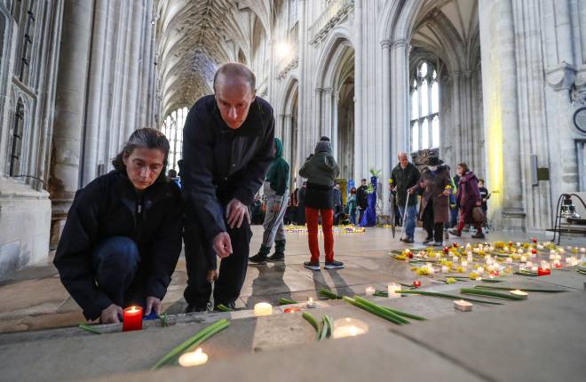 Candles and flowers are laid on the floor of Winchester Cathedral by a couple one of whom is kneeling and the other is standing