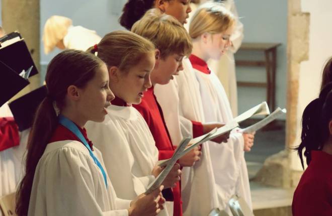 A line of choristers in robes singing from sheet music