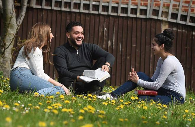 Young adults sitting on grass laughing with bible